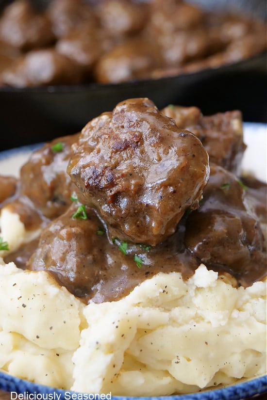 A close up of mashed potatoes and Salisbury steak meatballs and gravy.