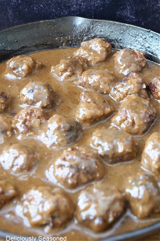 A cast-iron pan with Salisbury steak meatballs and gravy in it.