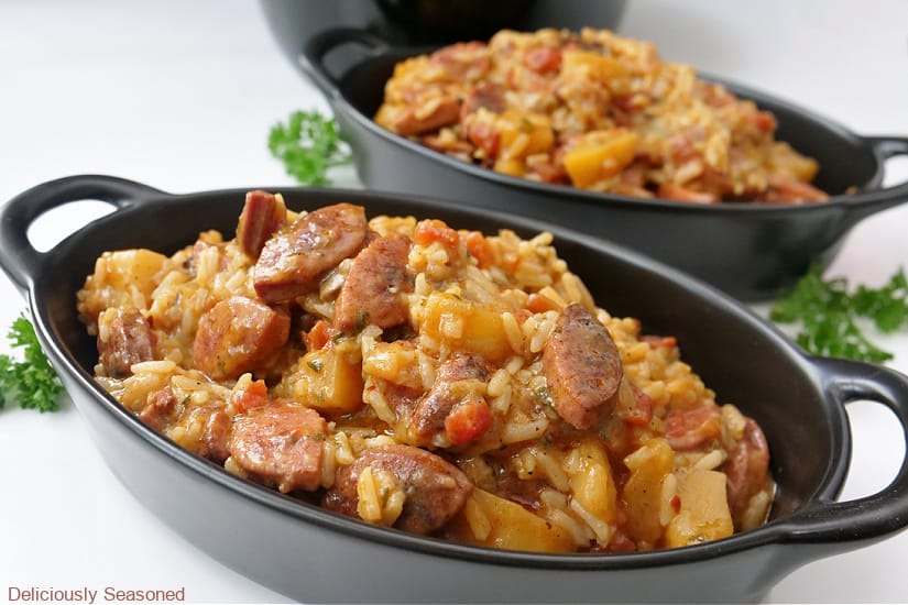 Two black oval bowls filled with sausage rice and potatoes.