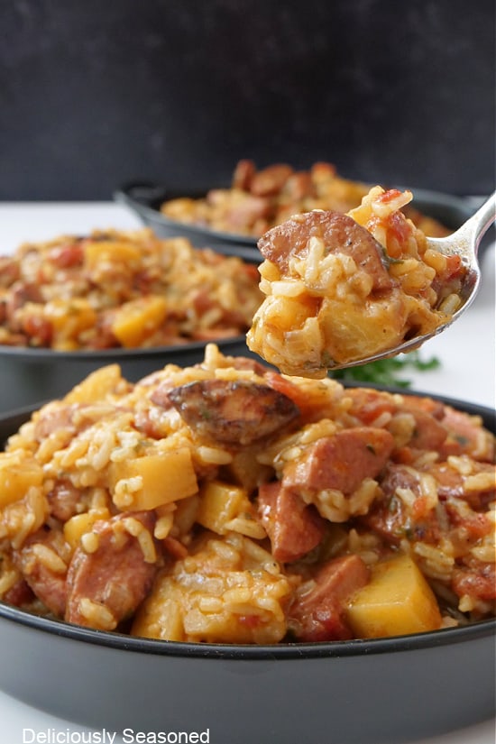 A spoonful of sausage, rice and potatoes held over a black oval bowl.