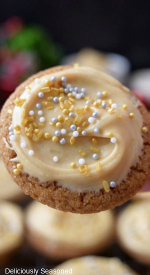 A close up of a mini frosted molasses cookie with frosting and candied sprinkles on it.