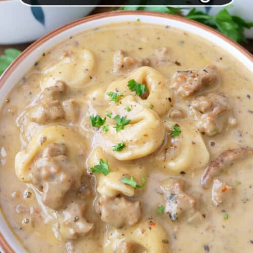 A white soup bowl filled with a serving of tortellini soup with Italian sausage.