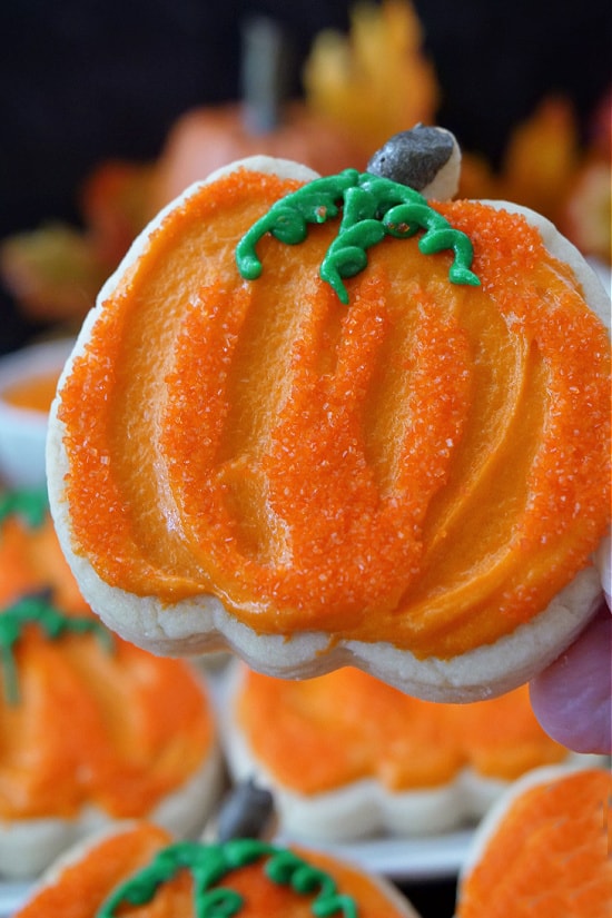 A close up of a pumpkin shaped cookie with orange frosting.