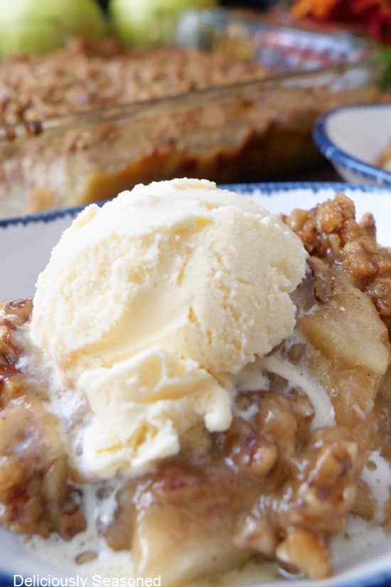 A scoop of vanilla ice cream on top of a serving of caramel apple crumble.