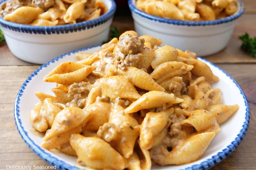 A horizontal photo of three serving bowls with blue trim filled with cheesy beef pasta.