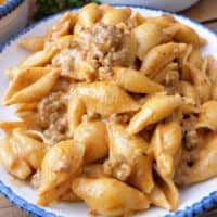 A close up of pasta shells and ground beef in a creamy sauce in a white bowl with blue trim.