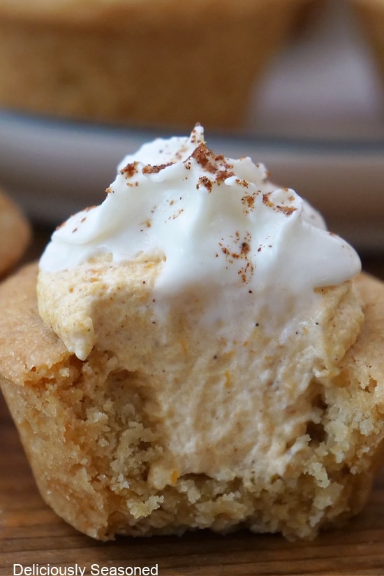 A close up of a bite-size sugar cookie cup filled with pumpkin mousse and topped with whipped cream that has a bite taken out.