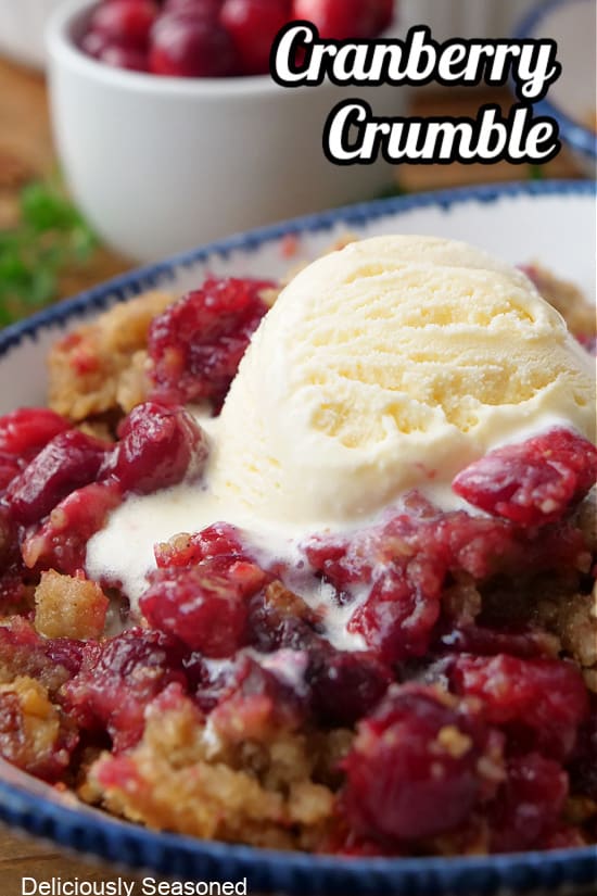 A white bowl with blue trim with a serving of cranberry crumble with a scoop of vanilla ice cream.