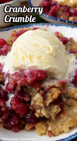 A white bowl with blue trim filled with a serving of cranberry crumble with a scoop of vanilla ice cream on top.