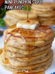 A round white plate with blue trim with a mini stack of pumpkin spice pancakes with a pad a butter and syrup being poured over the top.