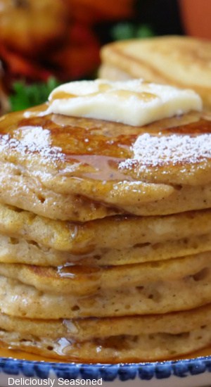 A close up of a stack of pumpkin pancakes with butter, syrup and powdered sugar on top.