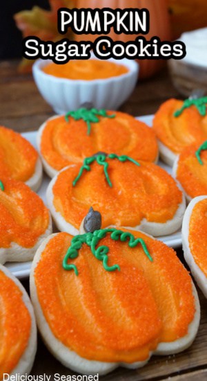 A white plate with pumpkin shaped cookies with orange frosting on them.