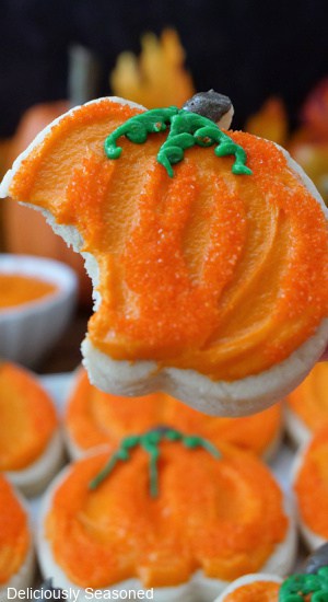 A close up of a pumpkin sugar cookie with a bite taken out of it.