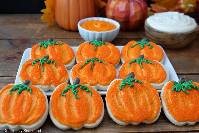A horizontal photo of 10 pumpkin cookies with orange frosting.