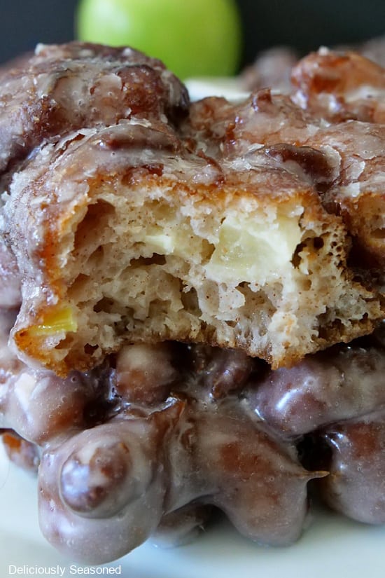 A super close up photo of two apple fritters with one having a bite taken out of it.