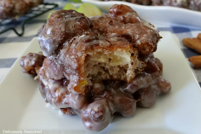 Close up photo of two apple fritters on top of each other with a bite out the fritter on the top, both placed on a white plate.