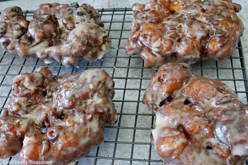 Four apple fritters on a wire rack.