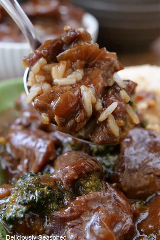 A close up of a spoon filled with a big bite of rice with beef and broccoli on it.
