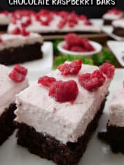 White plates with slices of chocolate raspberry bars on them that have raspberry whipped cream and coarsely chopped raspberries on top.
