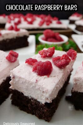 White plates with slices of chocolate raspberry bars on them that have raspberry whipped cream and coarsely chopped raspberries on top.