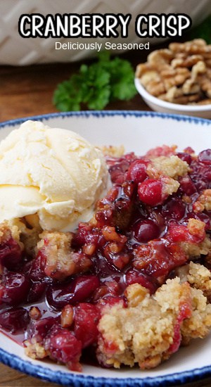 A white bowl with blue trim filled with cranberry crispy and a scoop of vanilla ice cream.
