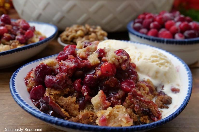 A horizontal photo of cranberry crisp in a white bowl with blue trim with a vanilla ice cream.