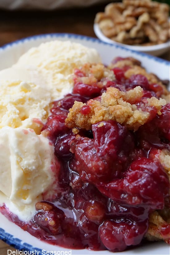 A close up of cranberry crisp and vanilla ice cream in a white bowl with blue trim.