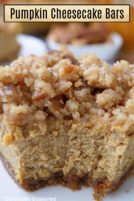 A close up of a pumpkin cheesecake bar, with a crunchy topping, with a bite taken out of it.