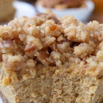 A close up of a pumpkin cheesecake bar, with a crunchy topping, with a bite taken out of it.