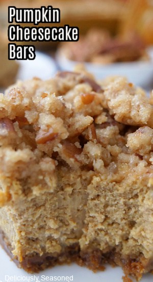 A close up of a pumpkin cheesecake bar with a crunchy topping with a bite taken out of it, and the title of the recipe at the top left corner.