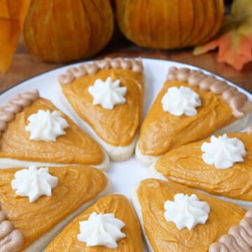 A white round plate with pumpkin pie shaped sugar cookies decorated like a slice of pumpkin pie.