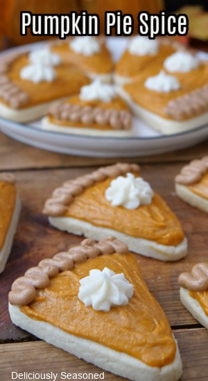 A wood surface with sugar cookies shaped like pumpkin pie on it with more on a white plate in the background.
