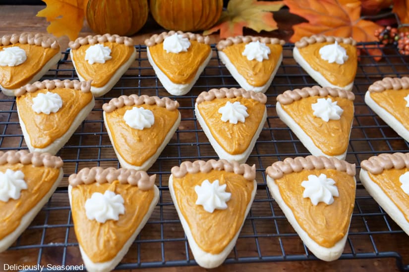 A wire rack with fifteen pie shaped sugar cookies on it decorated like pumpkin pie slices.