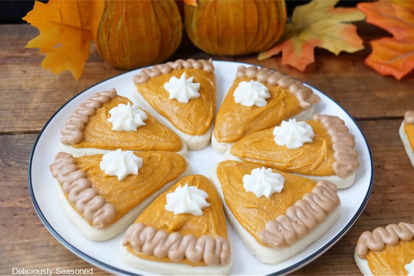 A horizontal photo of a white round plate on a wood surface with seven pie shaped sugar cookies on it.