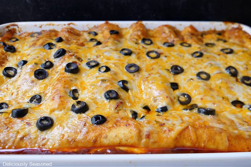A large white casserole dish filled with steak enchiladas with melted cheese and sliced black olives on top.