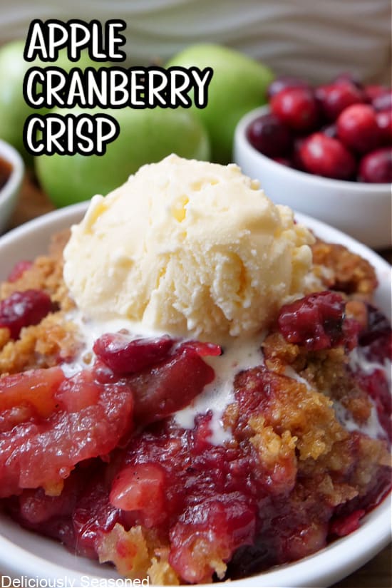 A close up of a white bowl filled with apple cranberry crisp with a scoop of vanilla ice cream on top.