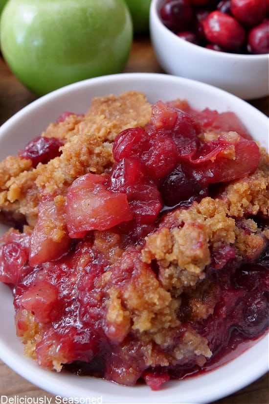 A close up of a white bowl filled with a serving of apple cranberry crisp.