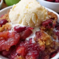 A close up of a serving of apple cranberry crisp with vanilla ice cream on top.