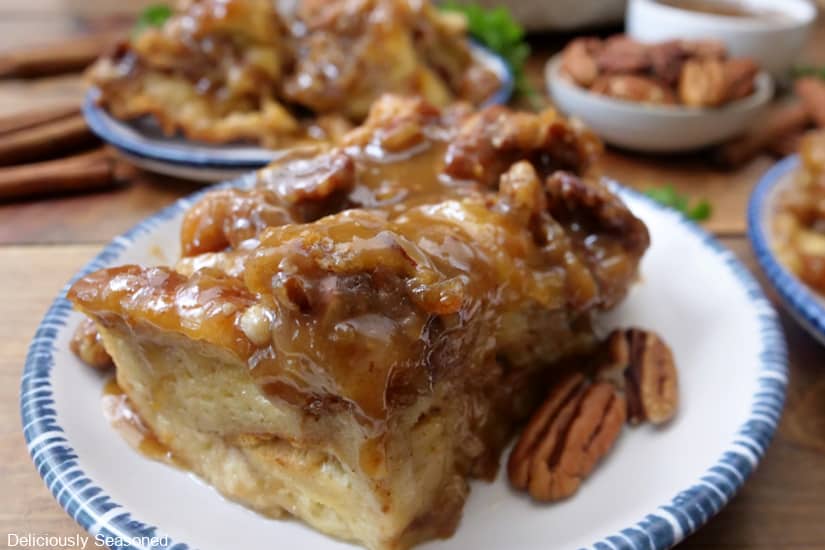 A horizontal photo of a serving of caramel bread pudding with a caramel drizzle on a round white plate with blue trim.