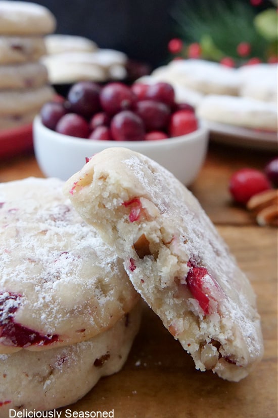 A close up of cranberry pecan sandie cookies with a bite taken out of one of them.