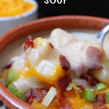 A close up of a bowl of potato soup with bacon, cheese, green onions.