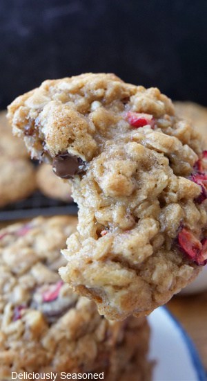 A close up of an oatmeal cookie with dark chocolate chips and fresh cranberries with a bite taken out of it.