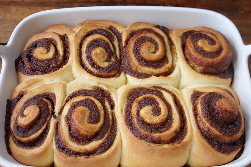 A white baking dish with eight baked cinnamon rolls in it.