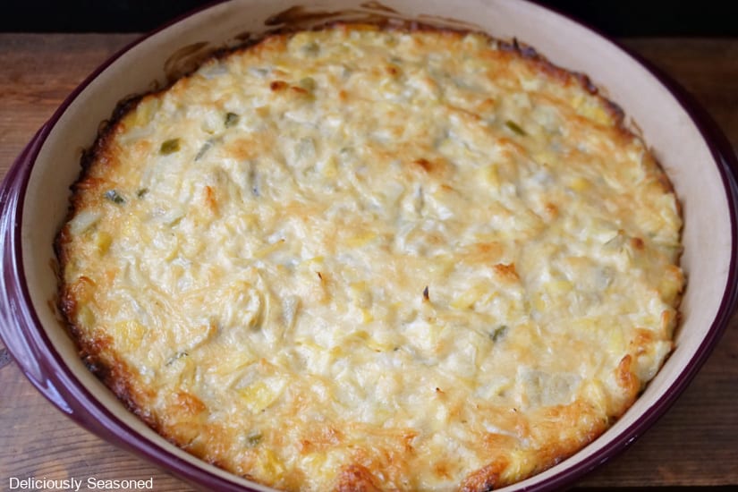 A horizontal photo of a round baking dish with artichoke dip in it after being pulled from the oven.
