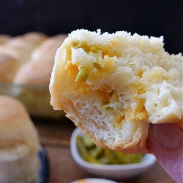 A jalapeno cheese dinner roll with a bite taken out held up close to the camera lens.
