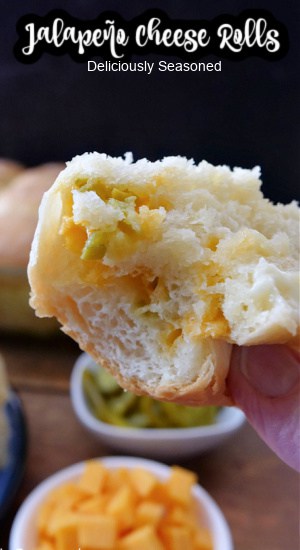 A close up of a dinner roll that has diced jalapenos and shredded cheddar cheese in it and a bite has been taken out of it.