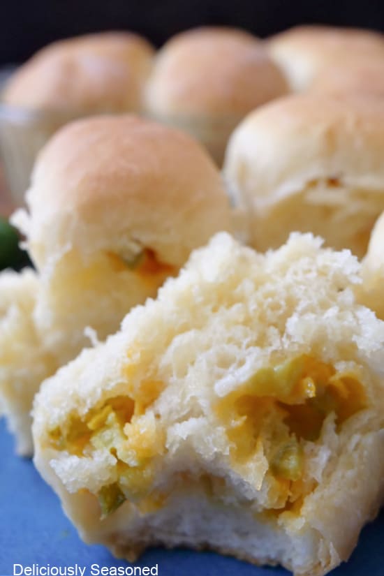 A close up of a dinner roll cut in half showing the melted shredded cheese and diced jalapeno in the dough with more dinner rolls in the background.