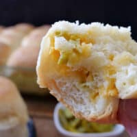 A close up of a dinner roll with a bite taken out of it showing the shredded cheddar cheese and diced jalapenos.
