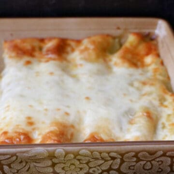 A tan baking dish filled with chicken enchiladas after being removed from the oven.
