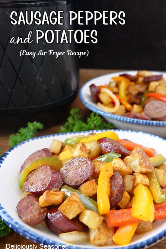 Two white bowls with blue trim filled with a serving of sausage, peppers and potatoes.